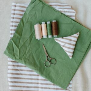 A flat lay of sewing tools and striped fabric with scissors and threads.